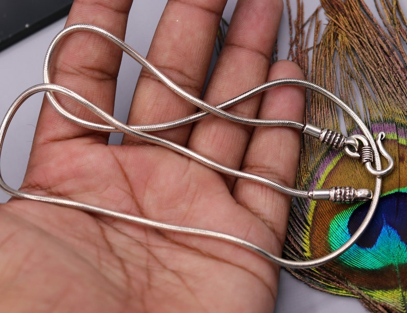 May include: A silver snake chain necklace with a clasp. The chain is thin and delicate, and the clasp is a simple hook.