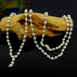 May include: A silver chain necklace with round beads. The necklace is displayed on a wooden surface.