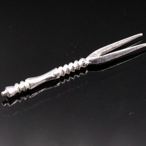 Puede incluir: Un tenedor de plata con un mango retorcido. El tenedor mide aproximadamente 15 cm de largo y tiene dos púas.