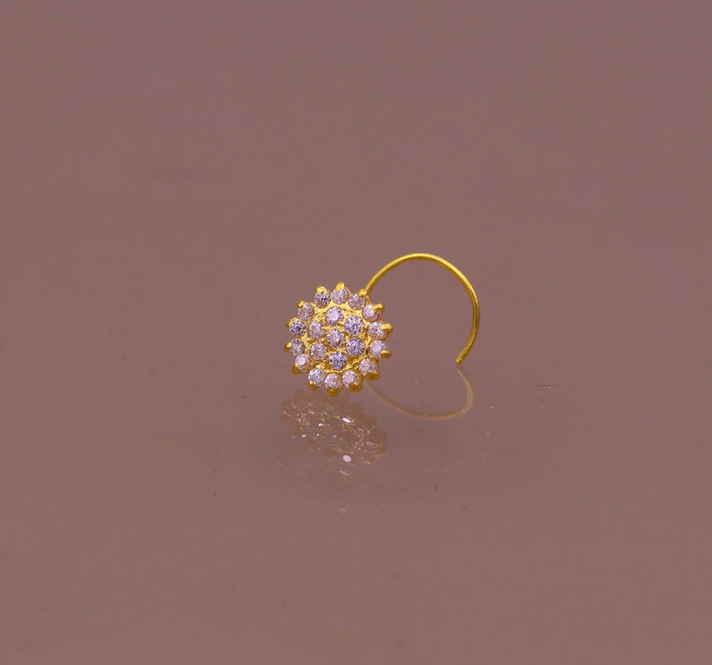 Puede incluir: Un aro de nariz de oro con un dise&ntilde;o redondo de cristal transparente.