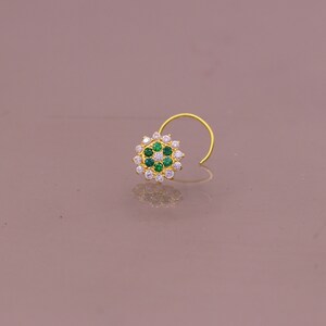 May include: A gold nose ring with a circular design featuring white and green gemstones.