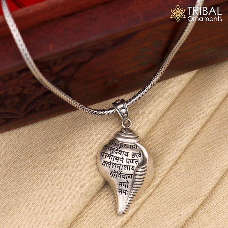 Op de afbeelding: Zilveren ketting met een schelp hanger met Sanskriet tekst. De hanger is gegraveerd met de woorden "Om  Kumbhaya  Gaurudbhavaya  Hary  Parmamalan  Pranat  Kaleshanashayat  Govidaya  Nama:"