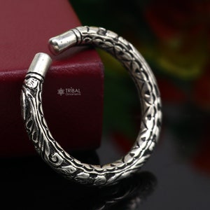 May include: A silver bangle bracelet with an intricate floral design. The bracelet is open and has a slightly curved shape.