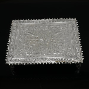 Puede incluir: Una bandeja decorativa de plata con un intrincado diseño floral. La bandeja tiene forma cuadrada y un borde elevado. Tiene cuatro patas y es perfecta para exhibir objetos pequeños.