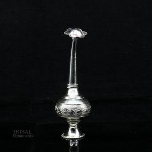 May include: A silver decorative spray bottle with an ornate design. The bottle has a long, slender neck and a flower-shaped top.