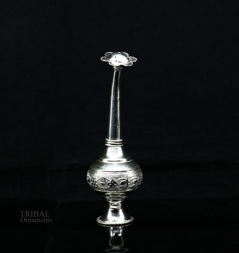 May include: A silver decorative spray bottle with an ornate design. The bottle has a long, slender neck and a flower-shaped top.