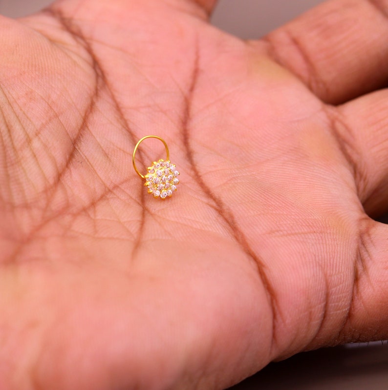 Puede incluir: Un aro para la nariz de oro con un dise&ntilde;o redondo de cristal transparente.