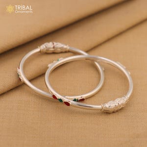 May include: Two silver bangles with decorative floral and beaded accents. The bangles have red and green enamel details. The text "TRIBAL Ornaments" is in the upper left corner.
