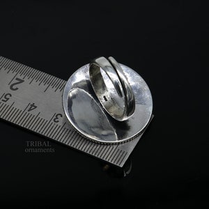 May include: Silver ring with a round design. The ring is being measured with a ruler, showing the size of the ring.