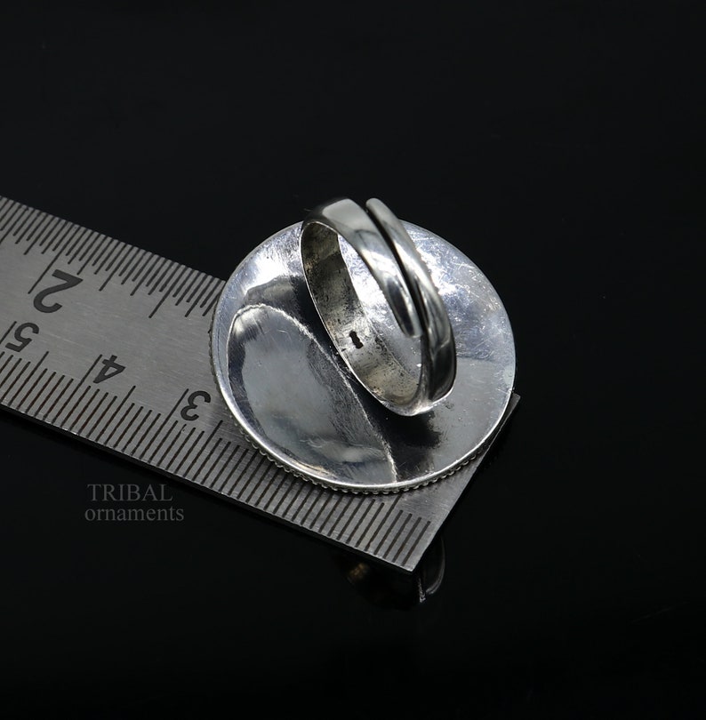 May include: Silver ring with a round design. The ring is being measured with a ruler, showing the size of the ring.