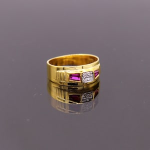 May include: A gold band ring with a square-shaped clear stone and two pink stones on either side.