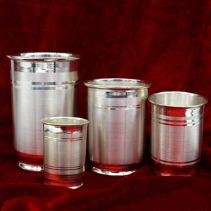 Op de afbeelding: Vier zilveren drinkbekers in verschillende maten, met een geborstelde afwerking en een decoratieve band rond het midden. De bekers staan op een rood fluwelen oppervlak.