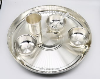 Op de afbeelding: Een zilveren servies met een grote ronde schotel, een hoge beker, twee kleine kommen en een kleine lepel. De set staat op een witte achtergrond.