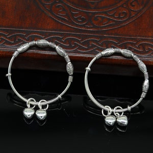 May include: Two silver bracelets with heart-shaped charms. The bracelets are made of thin silver wire and have a textured design. The charms are attached to the bracelets with small silver rings.