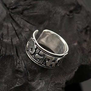 May include: A silver ring with an inscription of Sanskrit characters. The ring is open ended and adjustable.