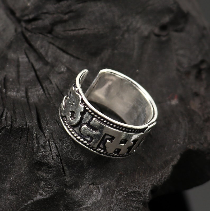 May include: A silver ring with an inscription of Sanskrit characters. The ring is open ended and adjustable.
