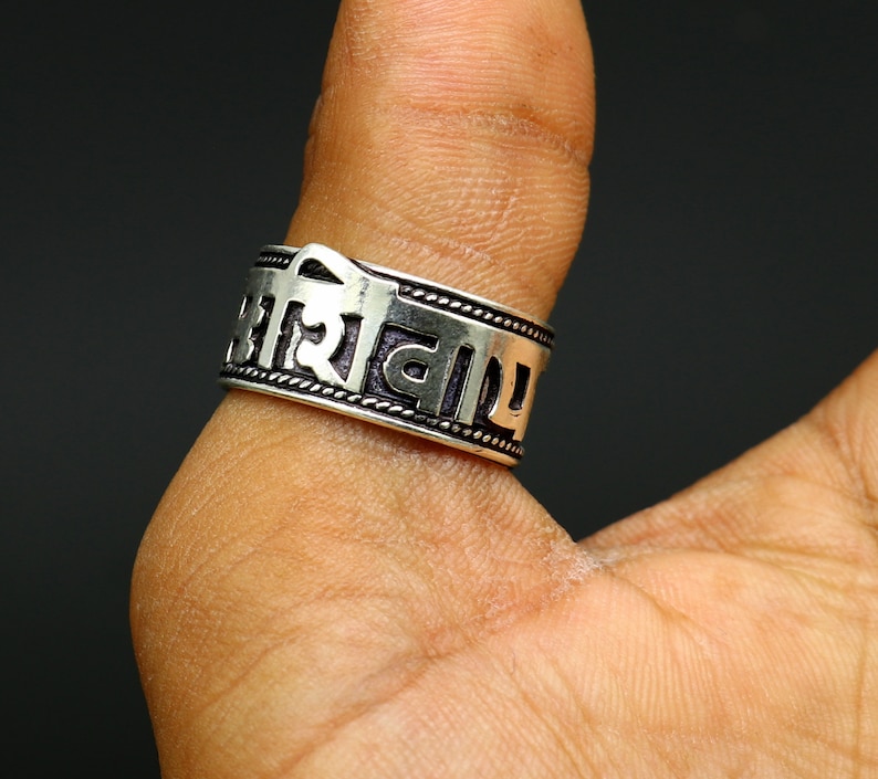 May include: Silver ring with a band of Sanskrit text. The ring is worn on a person's finger.
