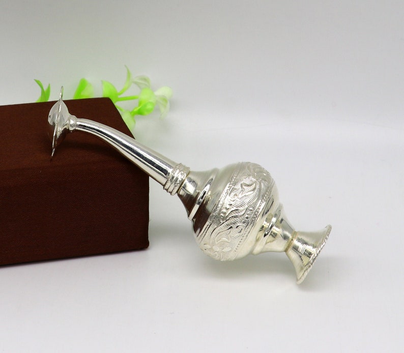 May include: A silver water sprinkler with intricate floral designs. The sprinkler has a long spout and a round base.