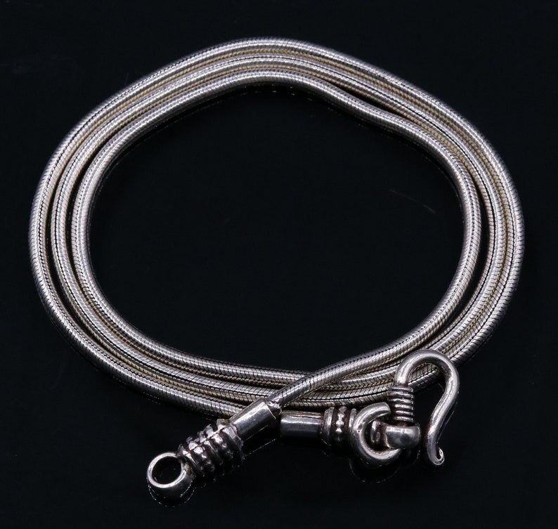 May include: A silver snake chain necklace with a silver clasp. The chain is made of multiple strands of silver wire that are twisted together.