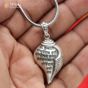 Op de afbeelding: Een zilveren ketting met een hanger in de vorm van een schelp met Sanskriet-schrift. De hanger is aan een zilveren ketting.