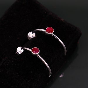 May include: A pair of silver hoop earrings with small red gemstone accents.