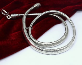 Può includere: Una collana a catena di serpente d'argento su uno sfondo di velluto rosso. La catena è realizzata con piccoli anelli intrecciati che creano un design liscio e fluido.
