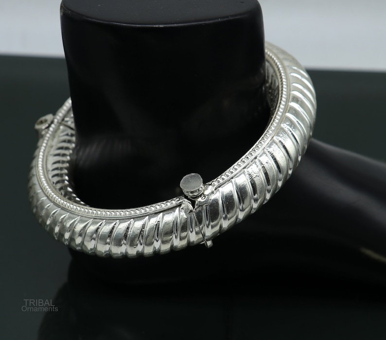 May include: A silver bangle bracelet with a textured design. The bracelet is open and has a hinged clasp.