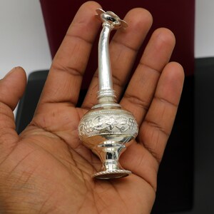 May include: A silver, ornate, decorative bottle with a floral design. The bottle has a long, thin neck and a round body. The bottle is decorated with intricate floral patterns.