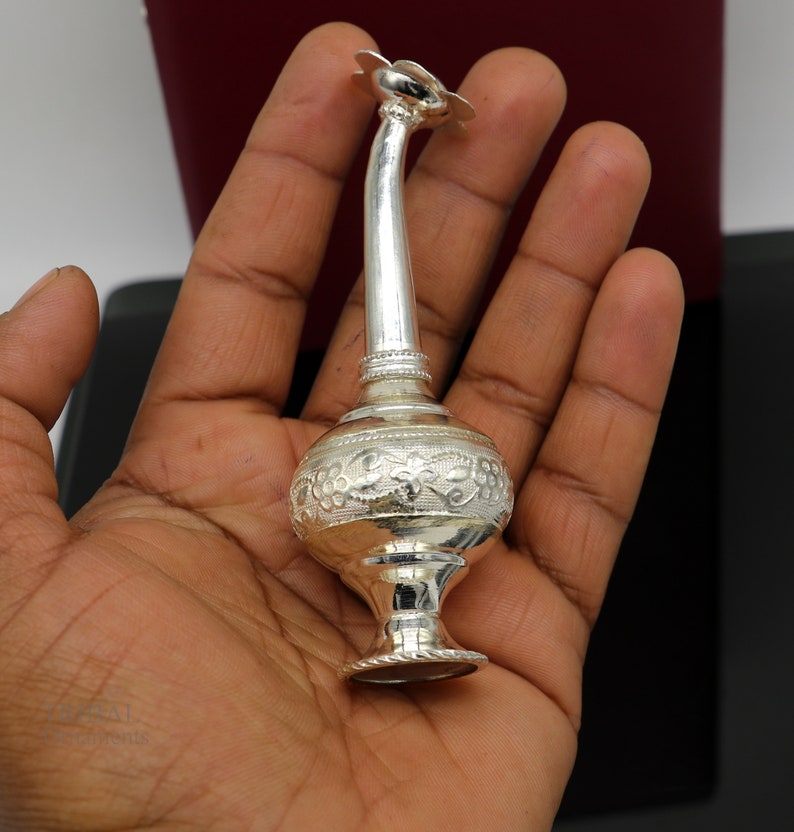 May include: A silver, ornate, decorative bottle with a floral design. The bottle has a long, thin neck and a round body. The bottle is decorated with intricate floral patterns.