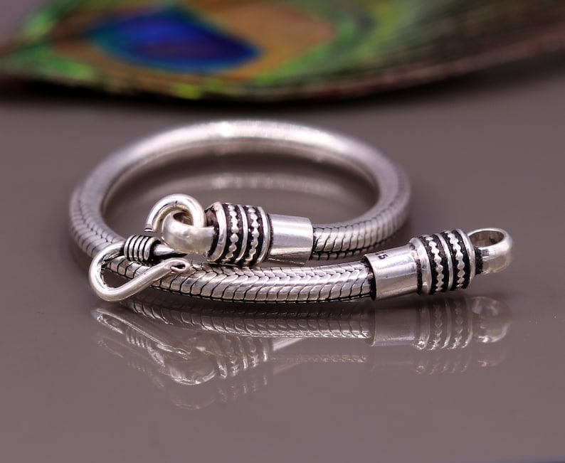 K&ouml;nnte beinhalten: Ein silbernes Schlangenkettenarmband mit einem Verschluss. Das Armband ist aus Sterlingsilber gefertigt und hat eine polierte Oberfl&auml;che.