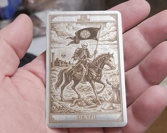 Può includere: Una carta metallica rettangolare con un'incisione della carta dei tarocchi della Morte. L'immagine raffigura uno scheletro a cavallo, con una bandiera con un fiore, con le parole "XIII DEATH" e "DEATH".
