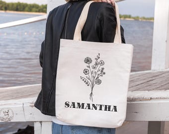 Könnte beinhalten: Eine weiße Canvas-Tragetasche mit schwarzem Blumendesign und dem Namen "SAMANTHA" in schwarzen Blockbuchstaben.