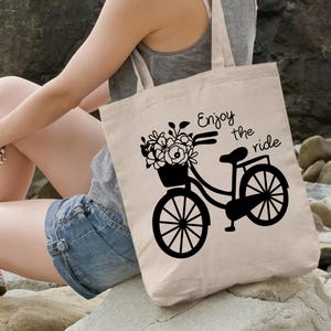 May include: A white canvas tote bag with black text and a bicycle graphic. The text reads "Enjoy the ride".