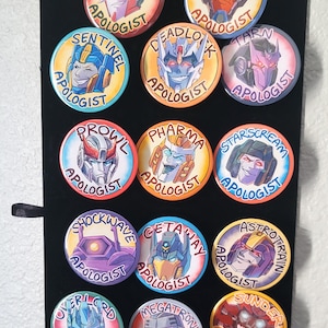 Può includere: Una collezione di bottoni rotondi e colorati con volti di robot stilizzati e la parola "APOLOGIST" in un design circolare. Ogni bottone presenta un nome di robot diverso, come "Knockout" e "Breakdown".