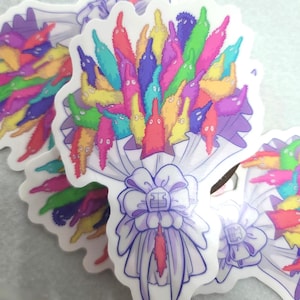 May include: A die-cut sticker featuring a bouquet of fuzzy, multi-colored worm toys in shades of pink, yellow, green, blue, and purple. The worms are arranged like flowers and wrapped in white paper with a large, light purple bow at the base.