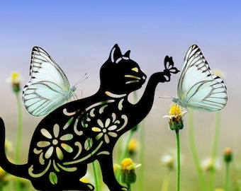 May include: A black metal silhouette of a cat with intricate floral designs reaching out to a white butterfly perched on a yellow flower.