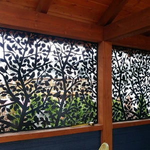 May include: Two black metal panels with a cut-out design of trees and birds. The panels are installed on a wooden frame and are set against a blue wall.