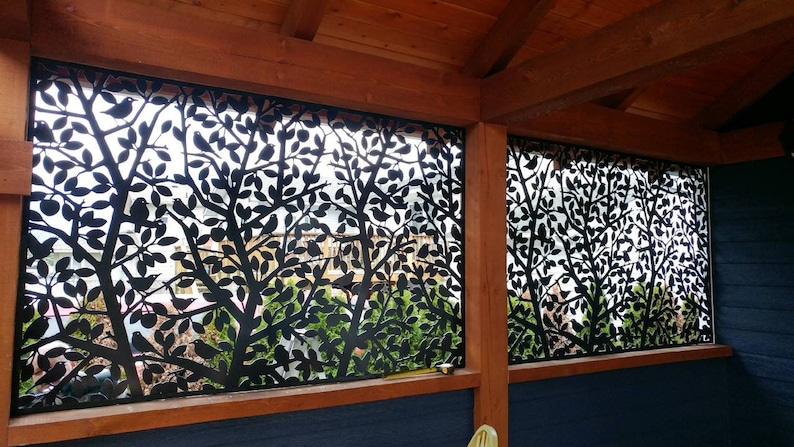 May include: Two black metal panels with a cut-out design of trees and birds. The panels are installed on a wooden frame and are set against a blue wall.