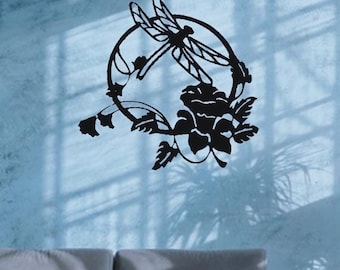 May include: Black metal wall art featuring a dragonfly within a circular frame, surrounded by floral and leaf accents. The dragonfly has detailed wing patterns. The artwork is mounted on a light blue wall.