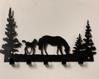 May include: Black metal key rack with a silhouette of a horse and foal in a forest setting. The rack has five hooks.