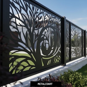 May include: Black metal fence panels with a tree design. The fence is installed on a concrete base with green grass and bushes in the foreground. The sky is blue. The text "METALCOART" is at the bottom.
