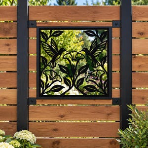 Peut inclure: Un panneau décoratif carré en métal noir présentant un motif découpé au laser de deux colibris se faisant face parmi des fleurs et des feuilles. Le panneau est fixé sur une clôture en bois et porte le texte 46 cm x 46 cm PANEL en bas.
