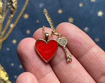 Peut inclure: Collier en or avec un pendentif en forme de cœur en émail rouge et un petit charme en forme de clé avec des strass transparents.
