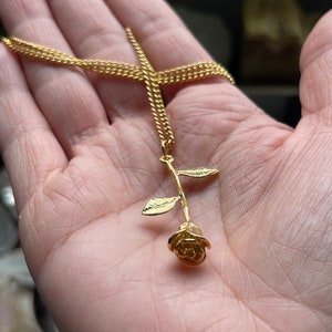 Peut inclure: Un collier en cha&icirc;ne dor&eacute;e avec un pendentif en forme de rose dor&eacute;e. La rose est d&eacute;taill&eacute;e avec une tige et des feuilles.