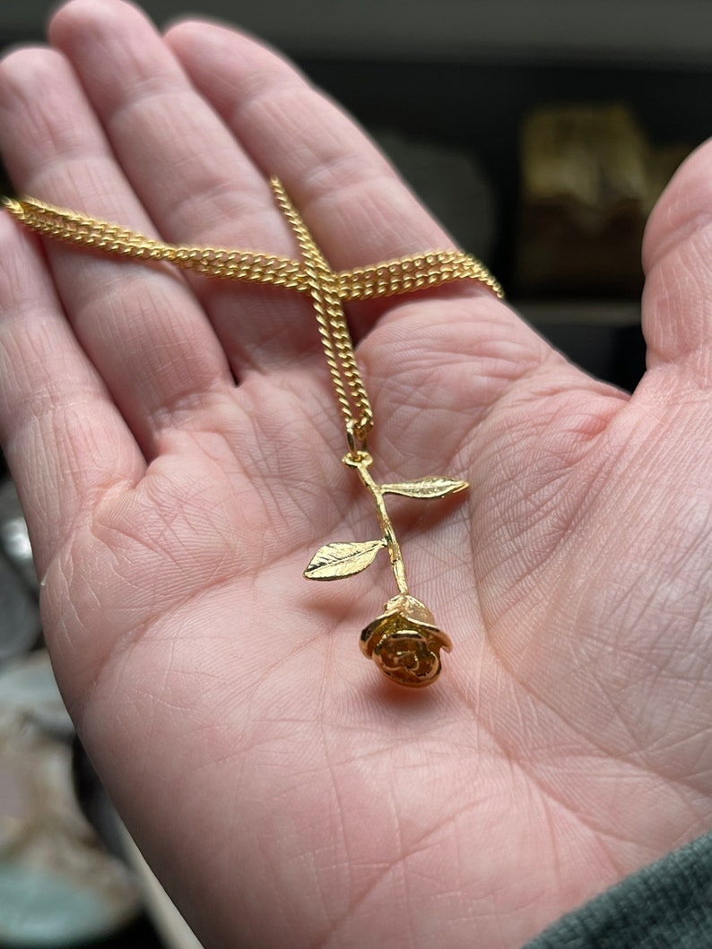 Peut inclure: Un collier en cha&icirc;ne dor&eacute;e avec un pendentif en forme de rose dor&eacute;e. La rose est d&eacute;taill&eacute;e avec une tige et des feuilles.