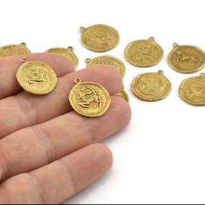 May include: A set of twelve gold-toned metal charms featuring zodiac signs. Each charm is circular and has a raised design of a zodiac symbol.