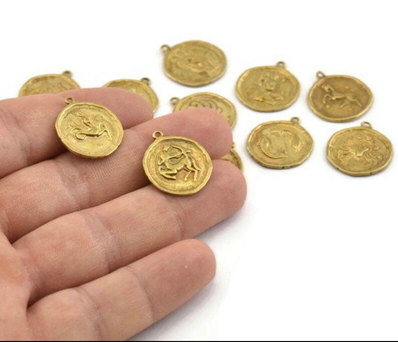 May include: A set of twelve gold-toned metal charms featuring zodiac signs. Each charm is circular and has a raised design of a zodiac symbol.