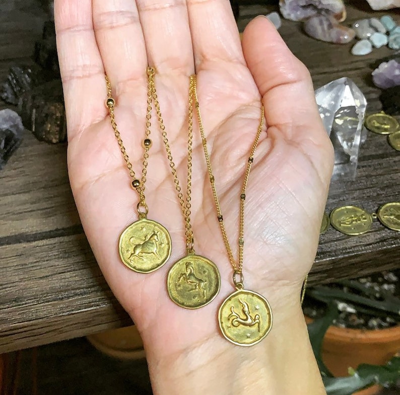 May include: Three gold necklaces with zodiac signs pendants. The pendants feature a bull, a goat, and a fish.