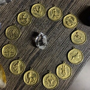 May include: Twelve gold-toned zodiac sign pendants with a crystal in the center. Each pendant features a different zodiac symbol.
