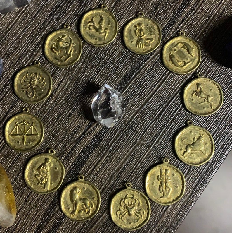 May include: Twelve gold-toned zodiac sign pendants with a crystal in the center. Each pendant features a different zodiac symbol.